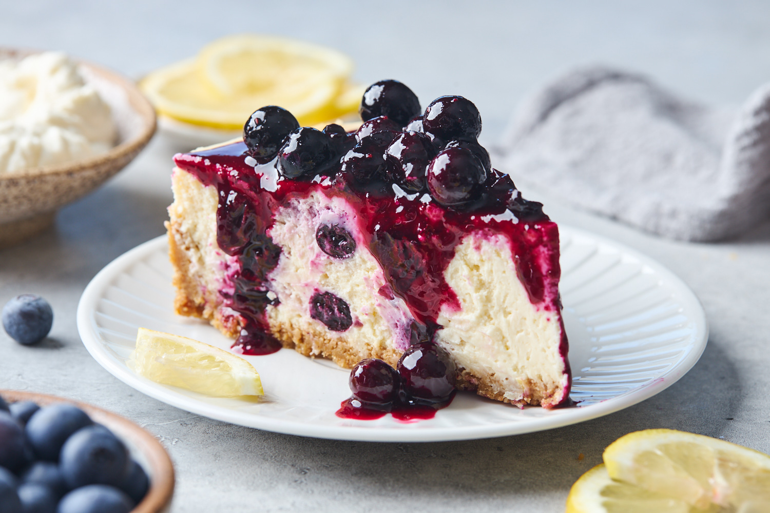 A slice of lemon blueberry cheesecake on a plate topped with fresh blueberries